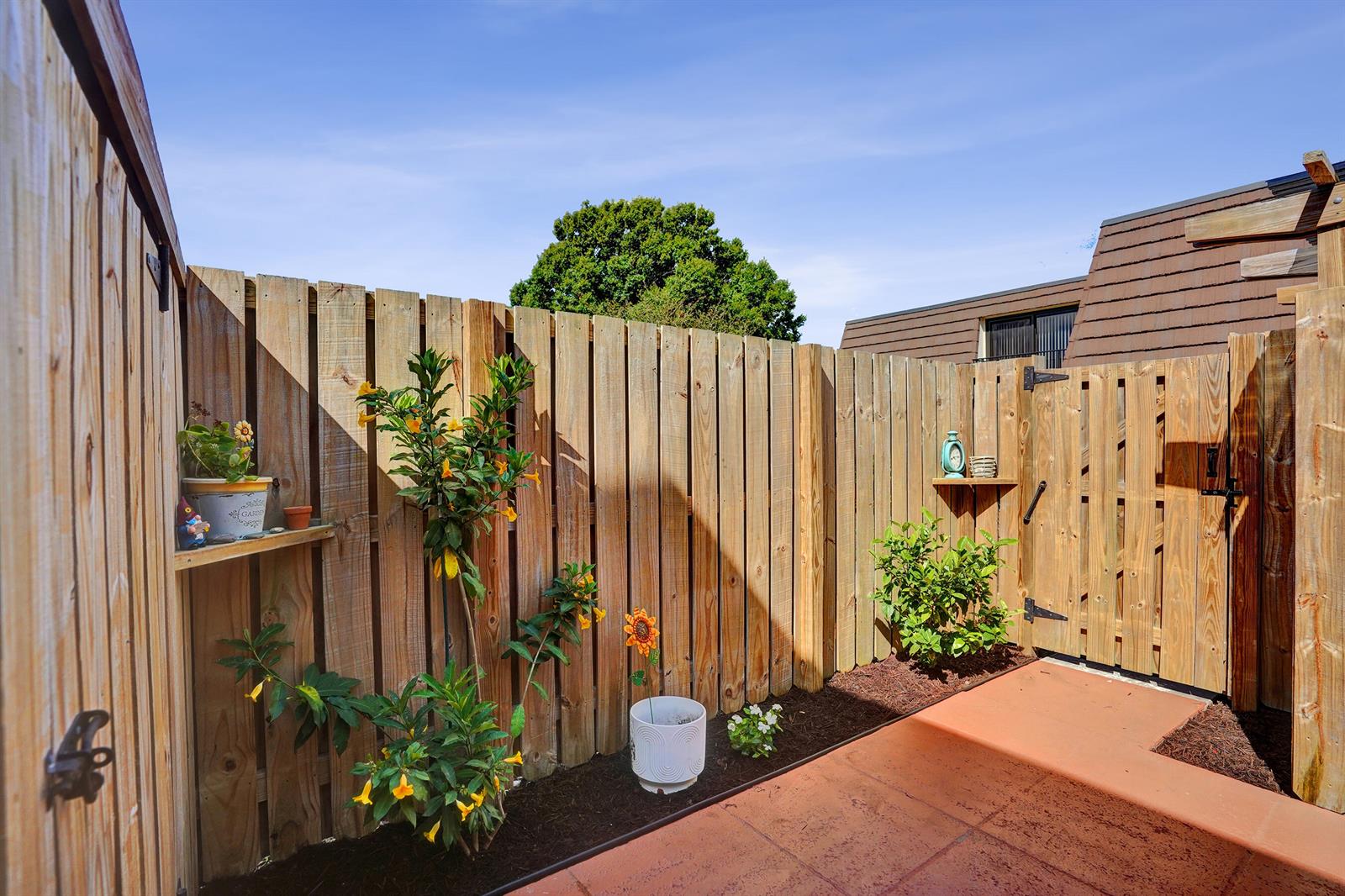 A fenced outdoor patio features a tiled floor, garden beds, and a wooden gate — 1126 11th Lane, Palm Beach Gardens FL 33418, PALM BEACH GARDENS, FL