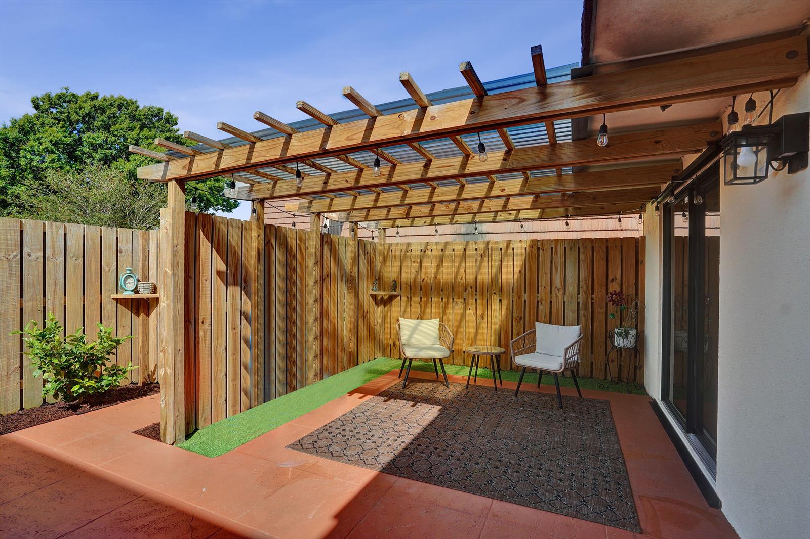 A patio features a wooden pergola, artificial turf, a patterned rug, and two chairs — 1126 11th Lane, Palm Beach Gardens FL 33418, PALM BEACH GARDENS, FL