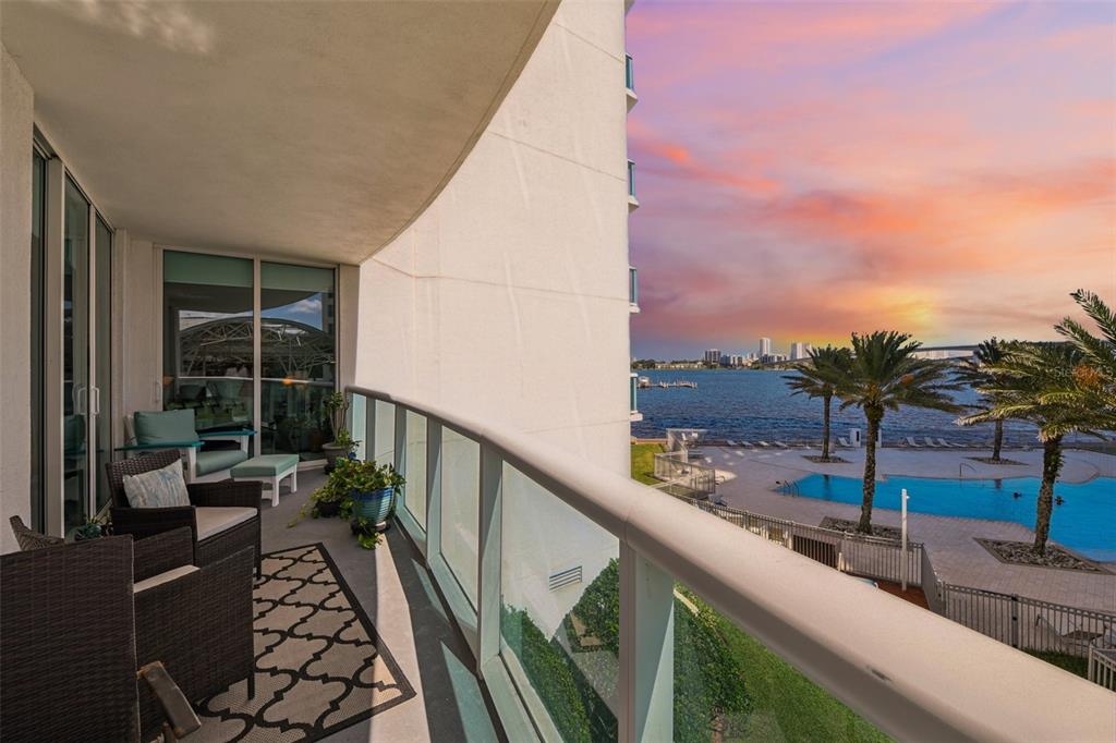 A balcony with outdoor furniture overlooks a swimming pool, a bay, and a distant city skyline — 241 RIVERSIDE DRIVE UNIT 305, DAYTONA BEACH, FL
