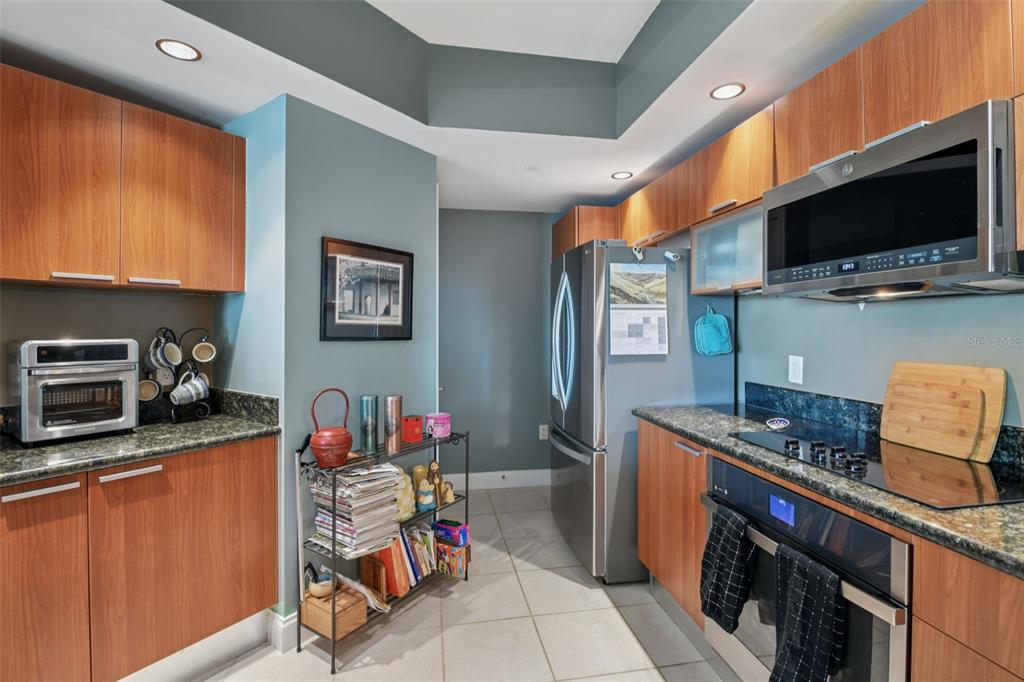 A kitchen features wood cabinets, granite countertops, stainless steel appliances, and blue-painted walls — 241 RIVERSIDE DRIVE UNIT 305, DAYTONA BEACH, FL