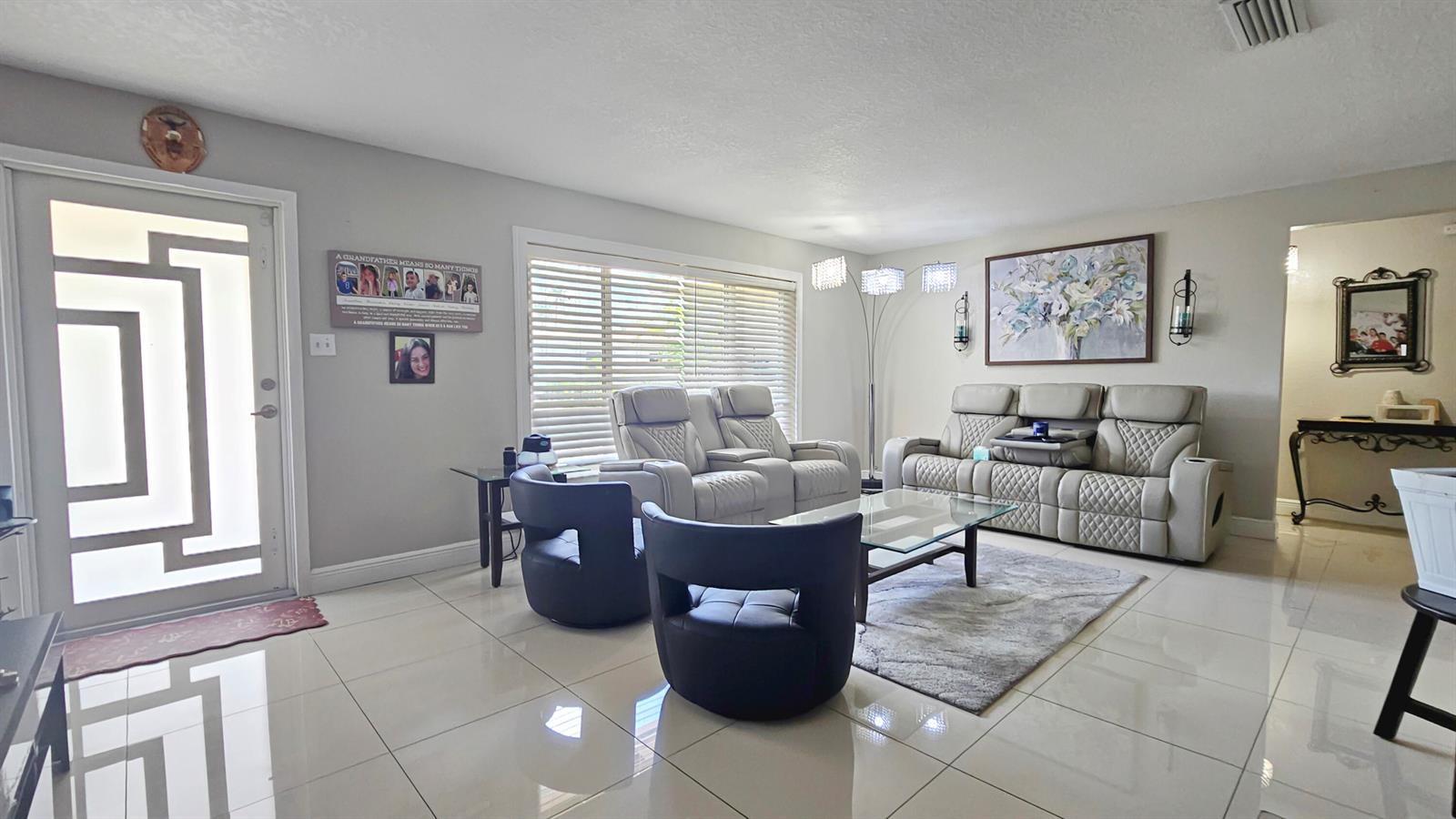 An empty living room features light-colored tile flooring, beige walls, and a modern front door — 7180 NW 10th Court, Margate FL 33063, MARGATE, FL