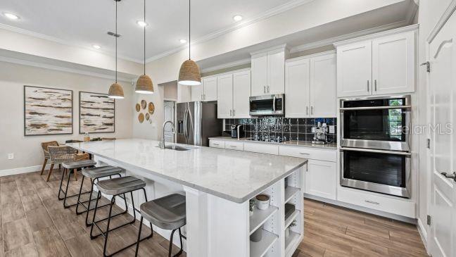 A modern kitchen features white cabinets, a large quartz island with bar seating, and stainless appliances — 9 LAURELCHERRY COURT, HOMOSASSA, FL