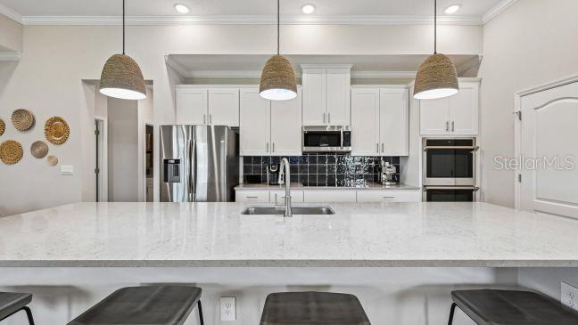 A kitchen features a large quartz island, white cabinetry, stainless steel appliances, and three pendant lights — 9 LAURELCHERRY COURT, HOMOSASSA, FL