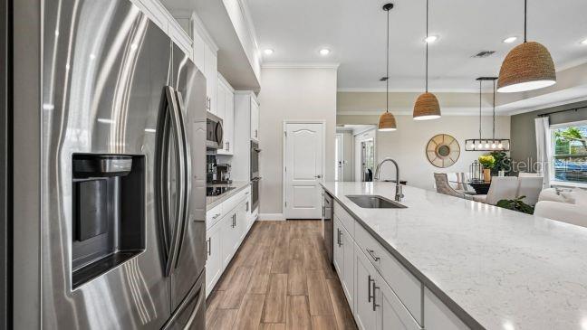 A modern kitchen features white cabinetry, a large quartz island, stainless steel appliances, and wood-look flooring — 9 LAURELCHERRY COURT, HOMOSASSA, FL