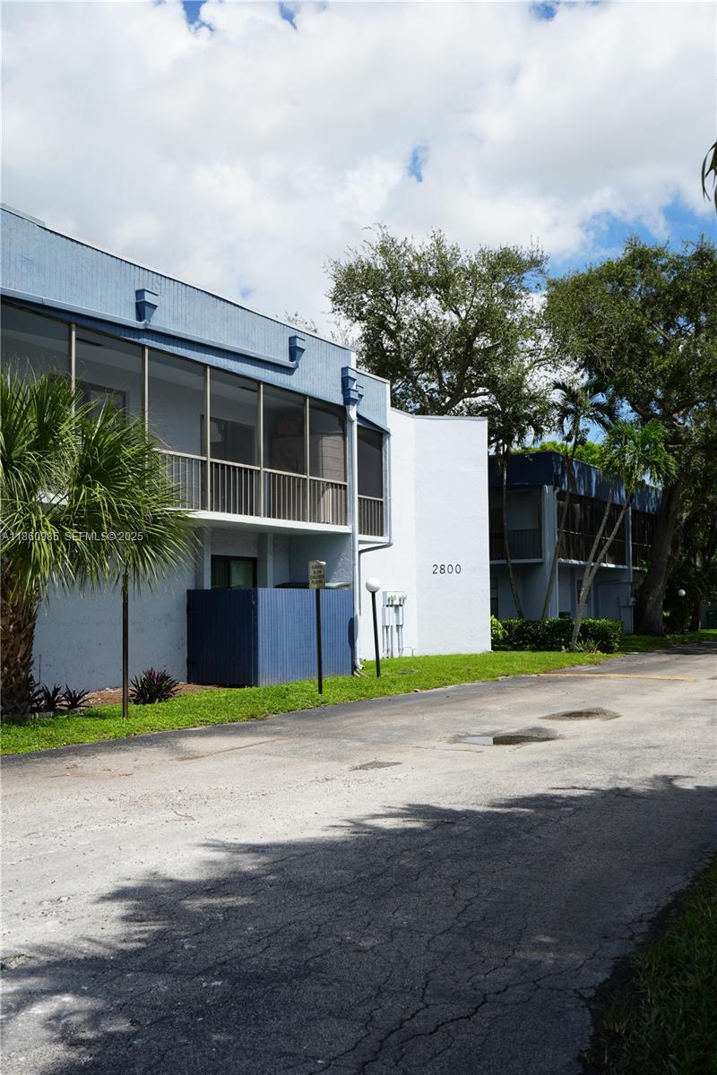 A two-story apartment building with blue trim and screened balconies sits beside a paved road — 2800 S University Dr # 2A, Davie FL 33328, DAVIE, FL