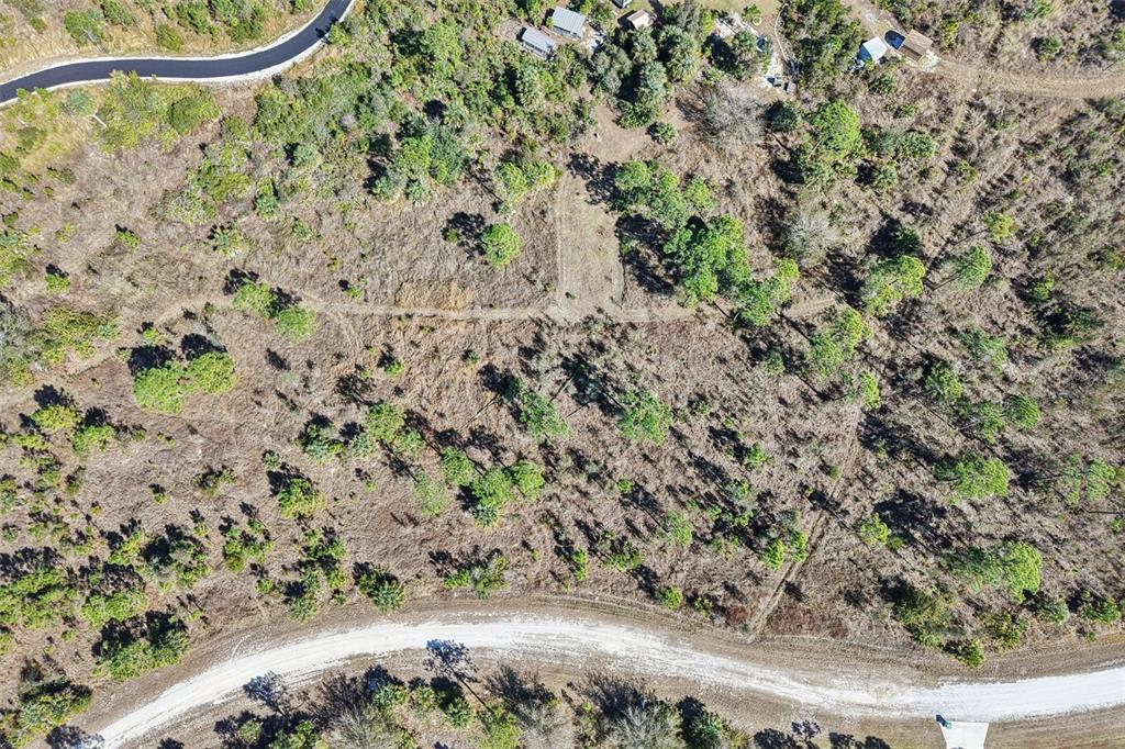 An aerial view shows a vacant, wooded lot bordered by a paved road and dirt path — 13588 CAROUSEL DRIVE, PUNTA GORDA, FL