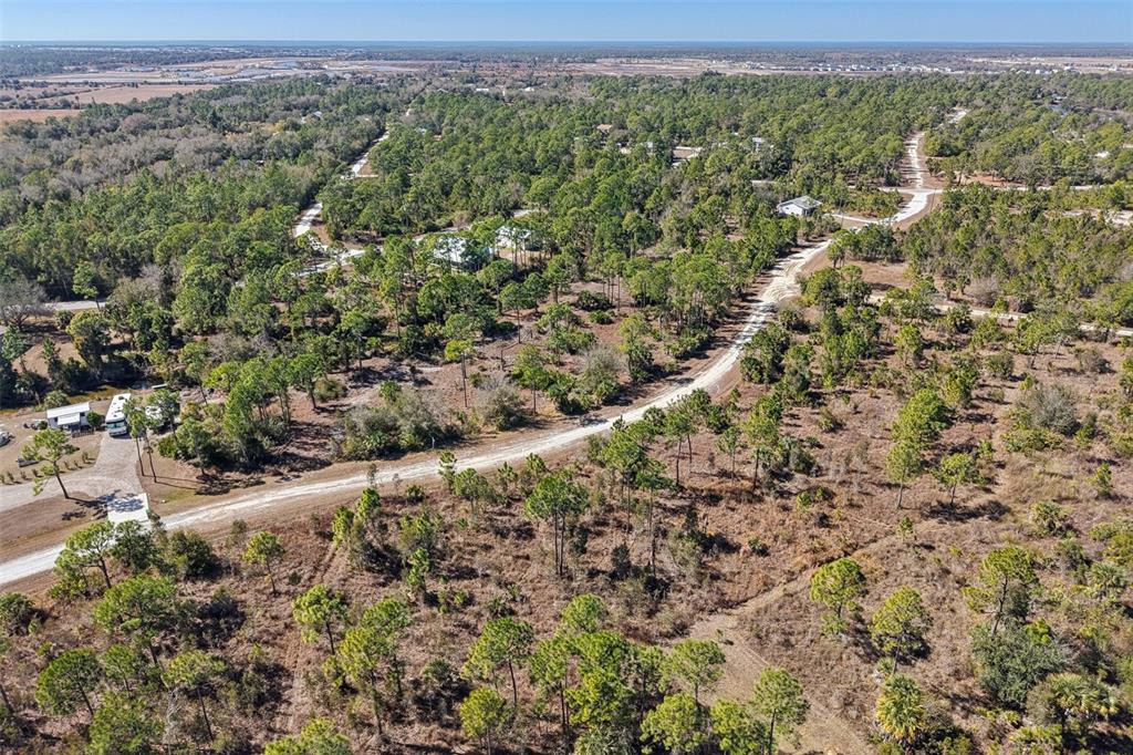 An aerial view shows a dirt road winding through a wooded, rural landscape with scattered houses — 13588 CAROUSEL DRIVE, PUNTA GORDA, FL