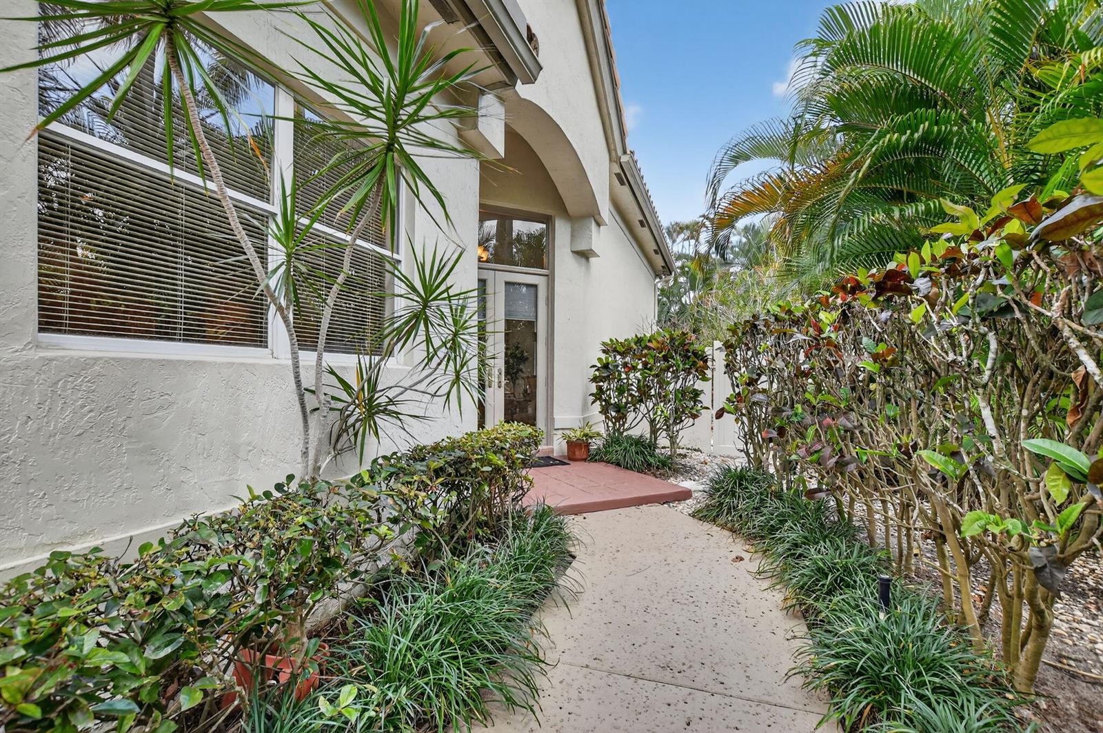 A concrete walkway leads to the glass front door of a house with tropical landscaping — 5184 NW 25th Way, Boca Raton FL 33496, BOCA RATON, FL