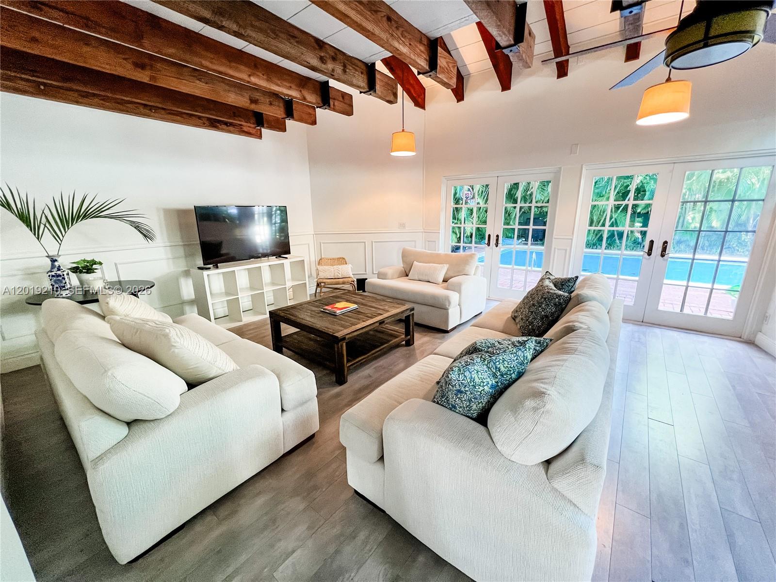 A living room features exposed wooden ceiling beams, white walls, and glass doors overlooking a pool — 320 W 55th St, Miami Beach FL 33140, MIAMI BEACH, FL