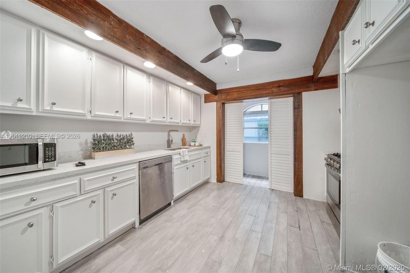A kitchen features white cabinetry, stainless steel appliances, wood ceiling beams, and light wood flooring — 320 W 55th St, Miami Beach FL 33140, MIAMI BEACH, FL