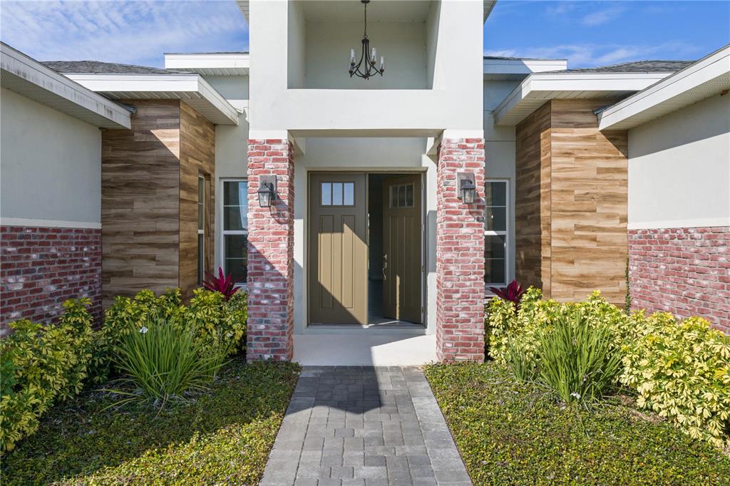 A front entrance with a brick-accented porch, wood-look siding, and a paved walkway — 208 SNOWY ORCHID WAY, LAKE ALFRED, FL