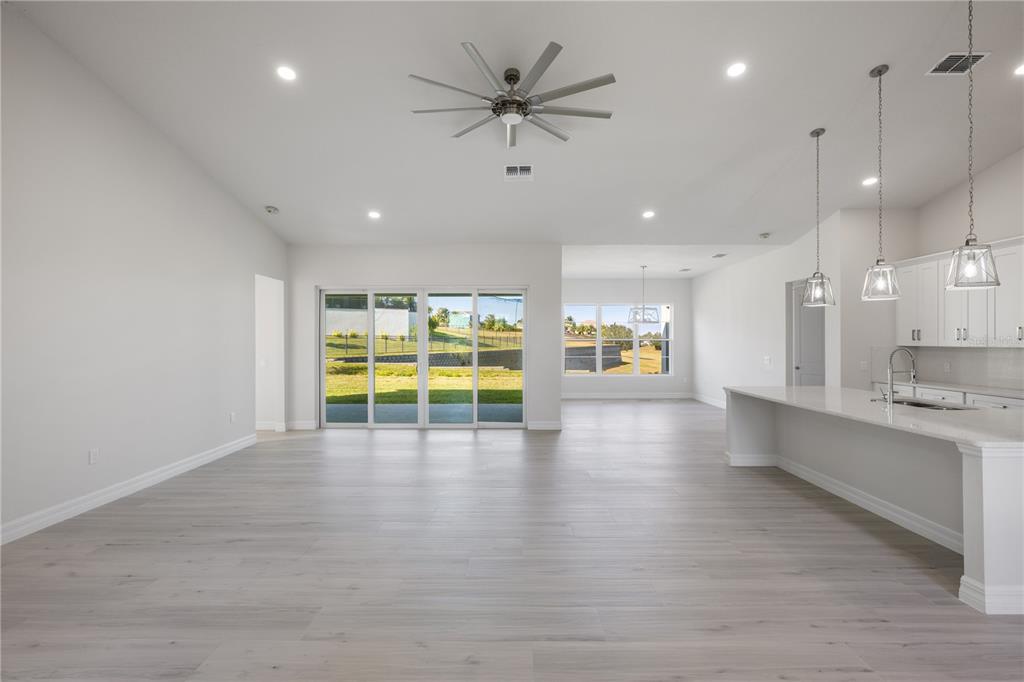 A bright, open-concept living area features light wood flooring, a ceiling fan, and kitchen island — 208 SNOWY ORCHID WAY, LAKE ALFRED, FL