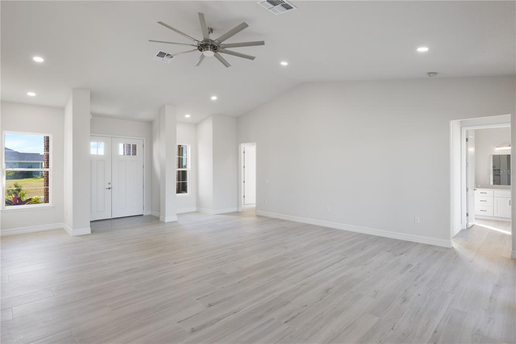 A bright, open-concept living area features light wood-look flooring, white walls, and a ceiling fan — 208 SNOWY ORCHID WAY, LAKE ALFRED, FL