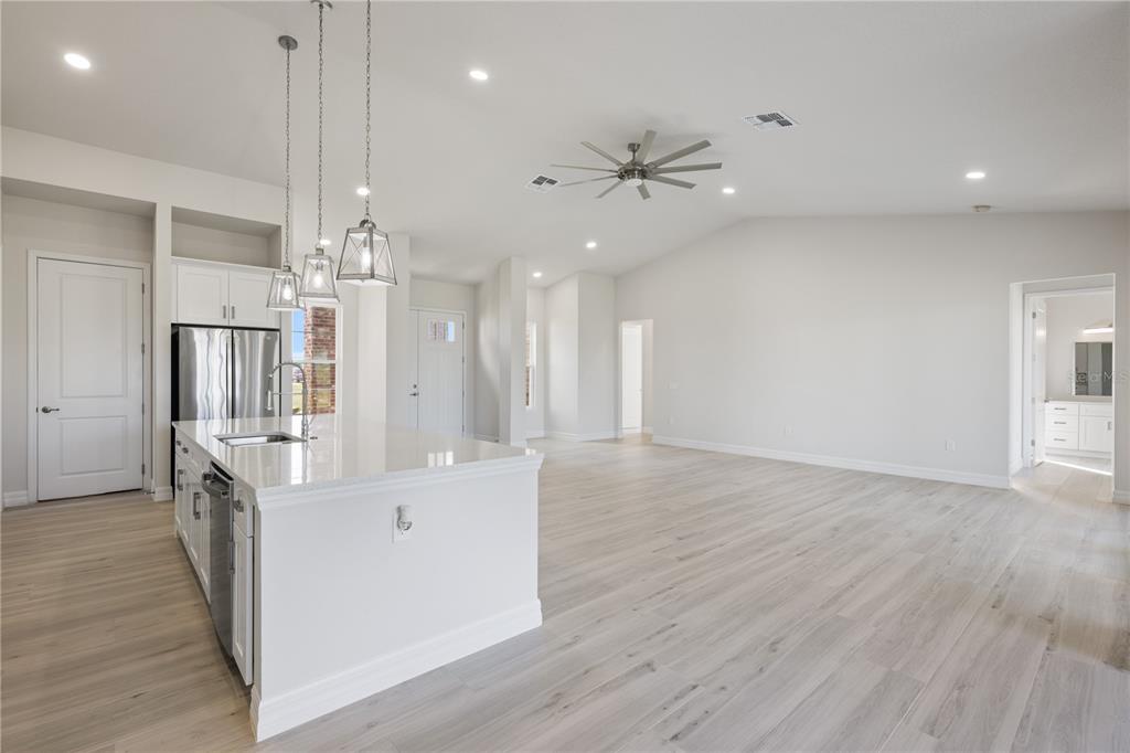 A modern kitchen with a white island and stainless steel appliances opens into a living area — 208 SNOWY ORCHID WAY, LAKE ALFRED, FL