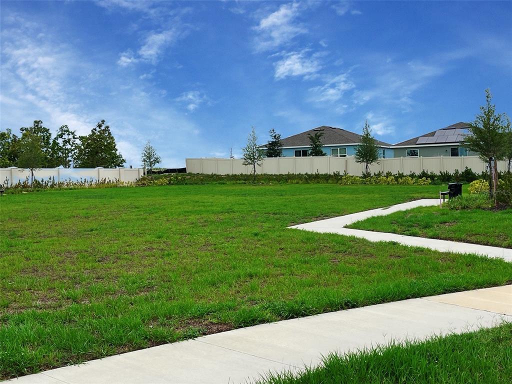 A grassy lot with a concrete sidewalk and a tan privacy fence in the background — 706 GINGER DRIVE, HAINES CITY, FL