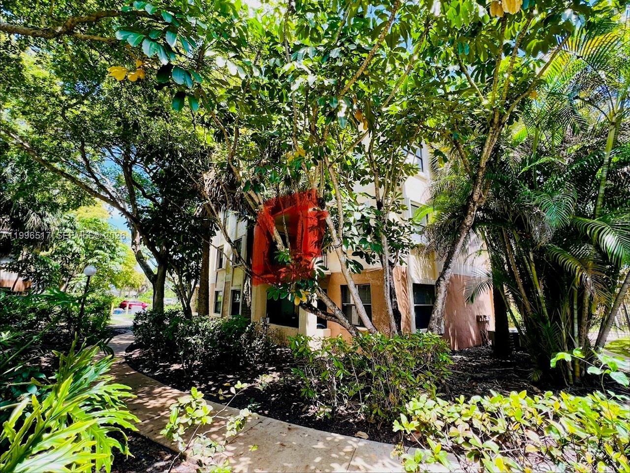 A multi-story apartment building exterior is partially obscured by lush trees and landscaping — 9999 Summerbreeze Dr # 214, Sunrise FL 33322, SUNRISE, FL