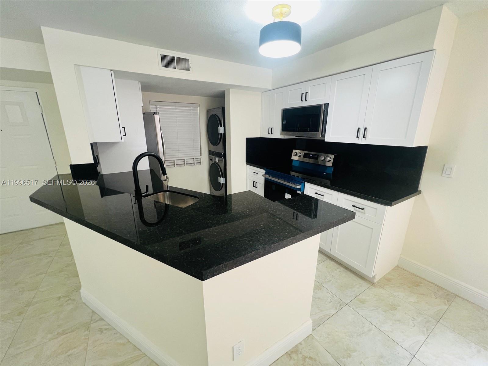 A kitchen features white cabinets, black countertops, a breakfast bar, and a stacked laundry unit — 9999 Summerbreeze Dr # 214, Sunrise FL 33322, SUNRISE, FL