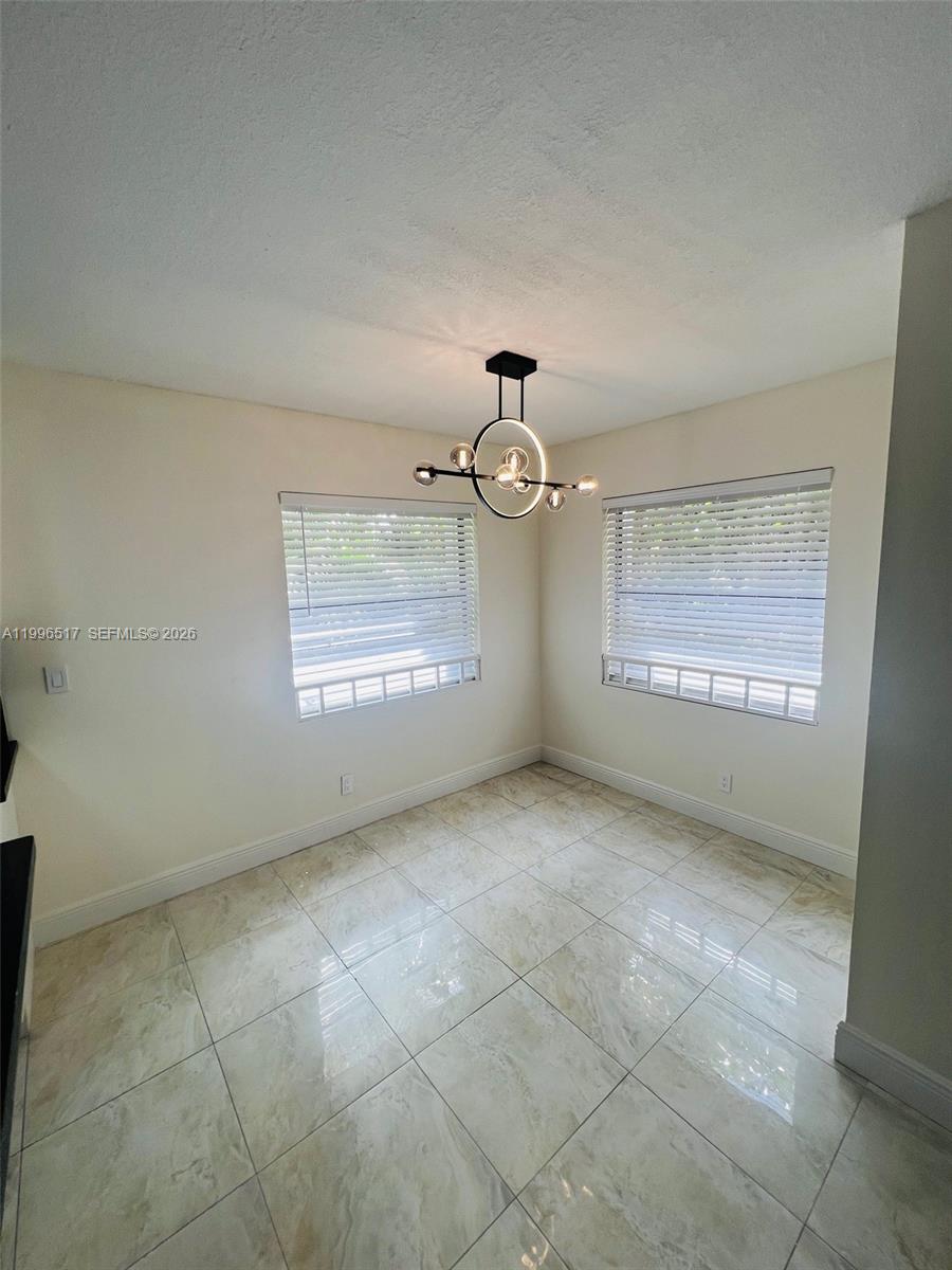 A dining area features light-colored tile flooring, two windows with white blinds, and a modern chandelier — 9999 Summerbreeze Dr # 214, Sunrise FL 33322, SUNRISE, FL