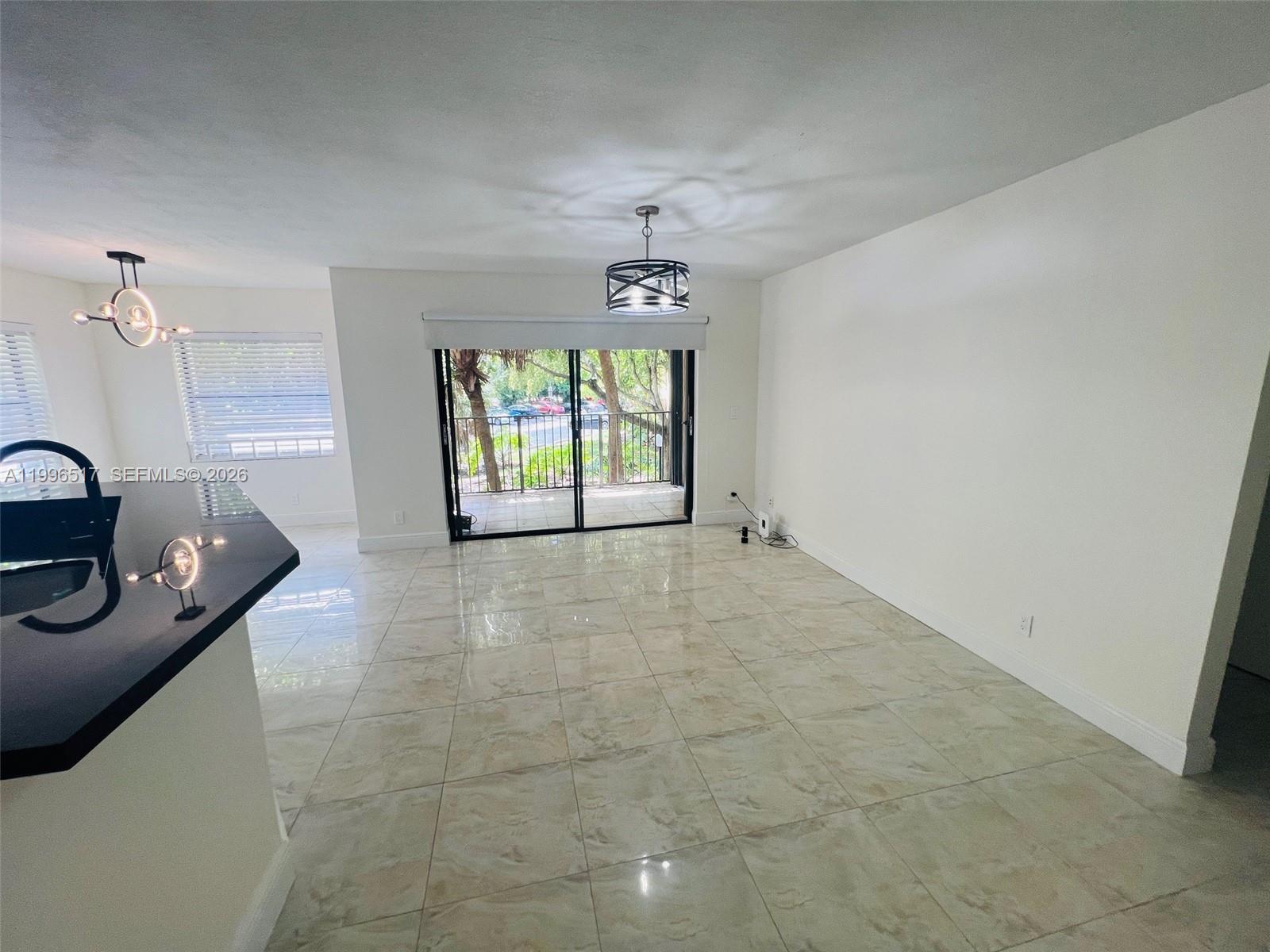 An open living area features light-colored tile flooring, white walls, and sliding glass balcony doors — 9999 Summerbreeze Dr # 214, Sunrise FL 33322, SUNRISE, FL
