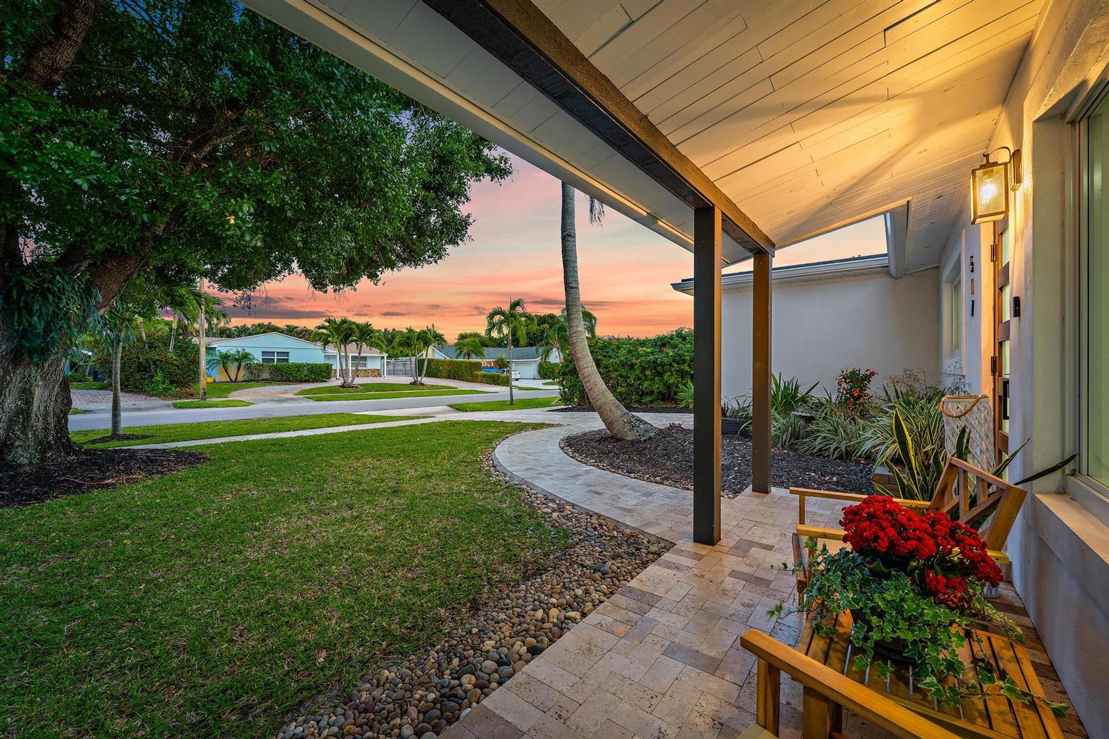 A covered porch with a wooden bench overlooks a front yard at sunset — 517 Gulf Road, North Palm Beach FL 33408, NORTH PALM BEACH, FL