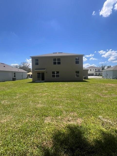 The rear exterior of a two-story house features a tan stucco facade and a lawn — 4037 BRADBURY WAY, SANFORD, FL