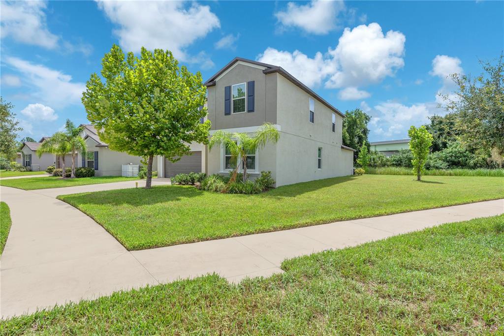 A two-story suburban house with a tan stucco exterior sits on a corner lot — 1911 FAN ALOE WAY, RUSKIN, FL
