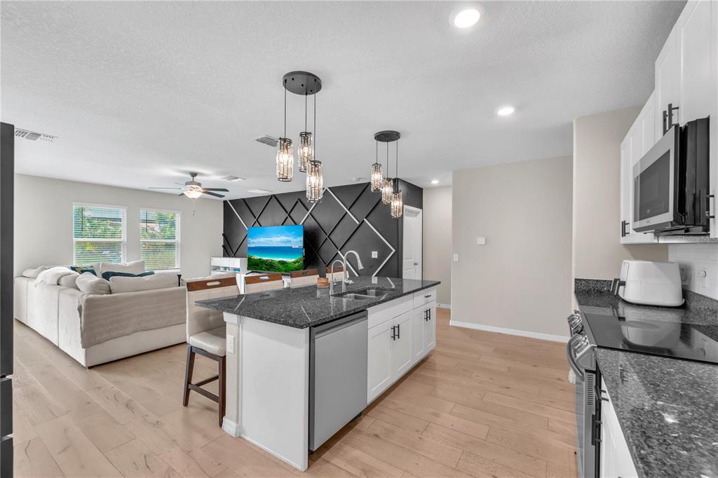 A modern kitchen with a granite island overlooks a living room with a black accent wall — 1911 FAN ALOE WAY, RUSKIN, FL