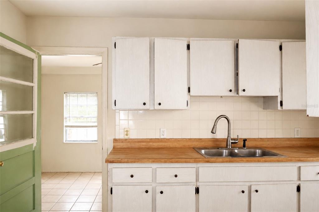 A kitchen features white cabinets, a wooden countertop, a stainless steel sink, and tiled backsplash — 1302 28TH STREET W, BRADENTON, FL