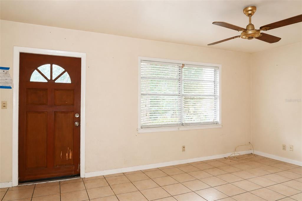 An empty room with beige walls, tile flooring, a wooden front door, and a ceiling fan — 1302 28TH STREET W, BRADENTON, FL