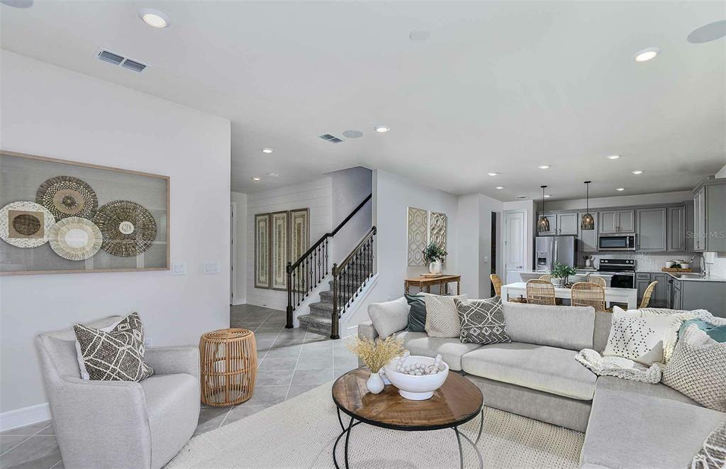 An open-concept living room features a staircase, gray cabinetry in the kitchen, and tile flooring — 11119 SYCAMORE GLEN LOOP, THONOTOSASSA, FL