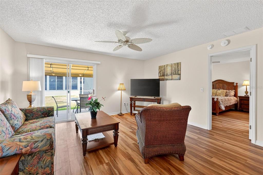 A living room with wood-look flooring, a floral sofa, wicker chair, and sliding glass doors — 1088 GENNESSE LANE, THE VILLAGES, FL