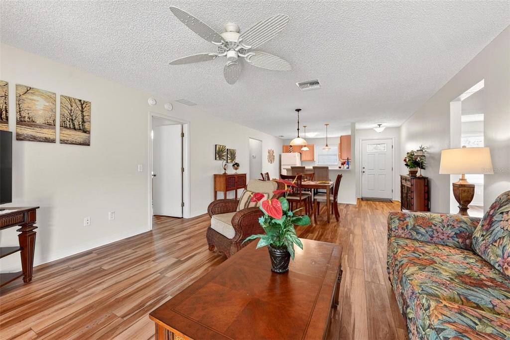 An open-concept living and dining area features wood-look flooring, a ceiling fan, and furniture — 1088 GENNESSE LANE, THE VILLAGES, FL
