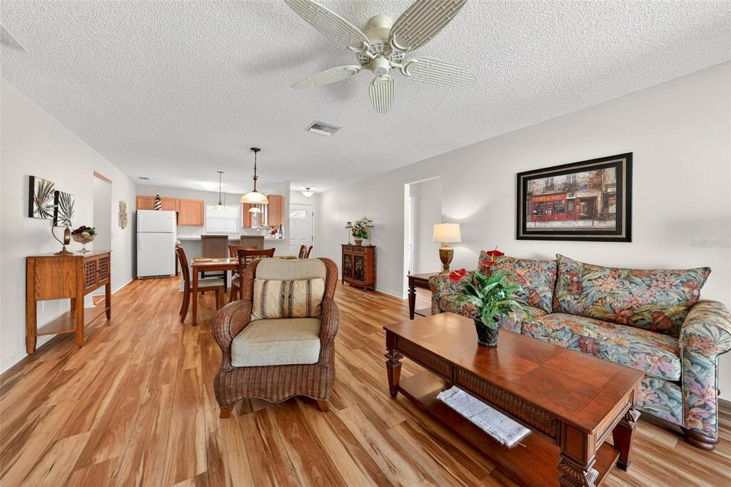 A living room and dining area with wood-look flooring, a floral sofa, and ceiling fan — 1088 GENNESSE LANE, THE VILLAGES, FL