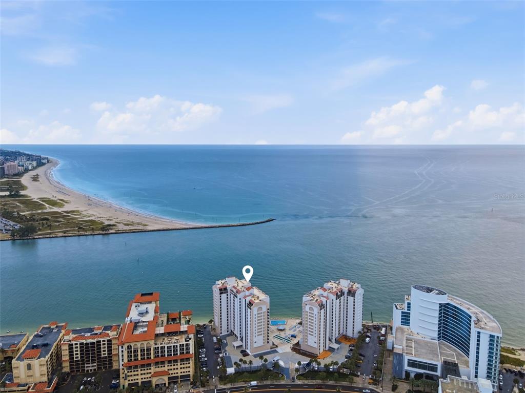 An aerial view shows a coastal high-rise building with a pool near the ocean — 450 S GULFVIEW BOULEVARD UNIT 705, CLEARWATER BEACH, FL