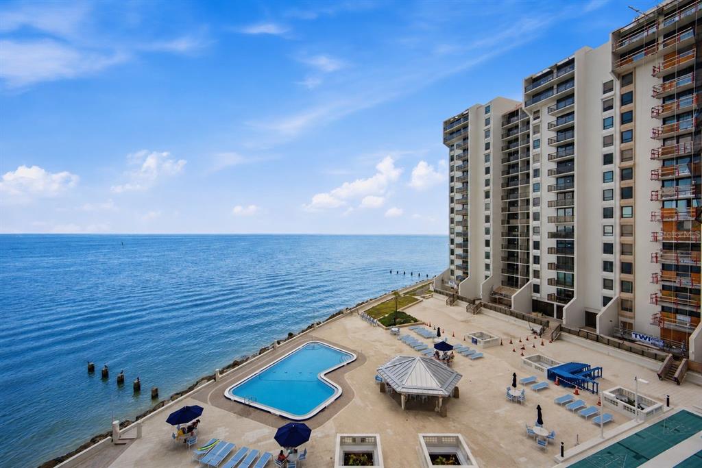 An elevated view of a coastal high-rise building with a swimming pool and patio area — 450 S GULFVIEW BOULEVARD UNIT 705, CLEARWATER BEACH, FL