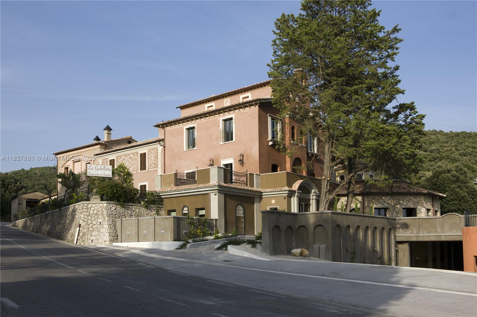 A multi-story, peach-colored building with a stone retaining wall sits beside a paved road — HOTEL FOR SALE UMBRIA ITALY, 0, 0