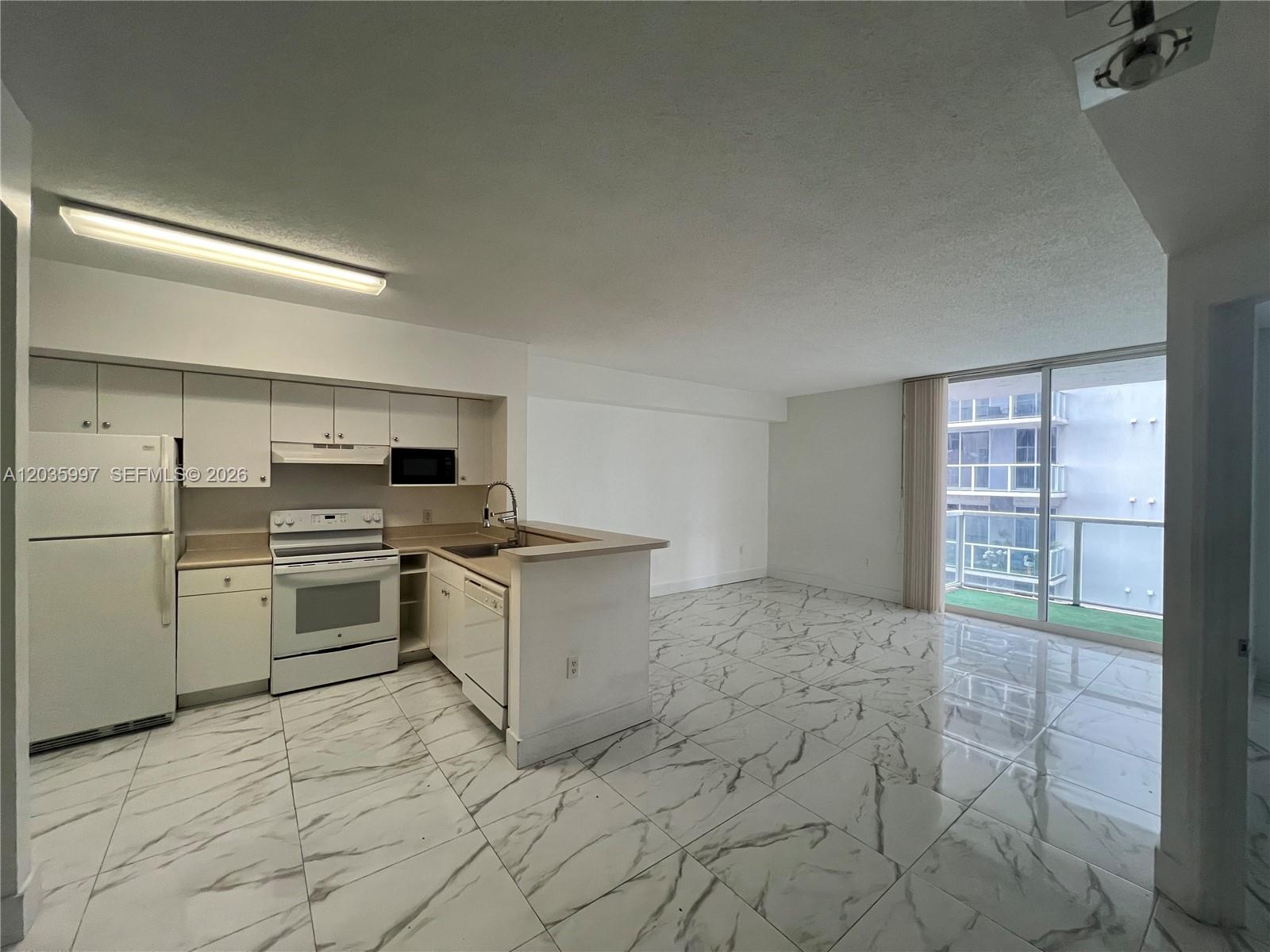 A kitchen with white cabinets and appliances opens into a living area with marble-patterned flooring — 5085 NW 7th St # 711, Miami FL 33126, MIAMI, FL