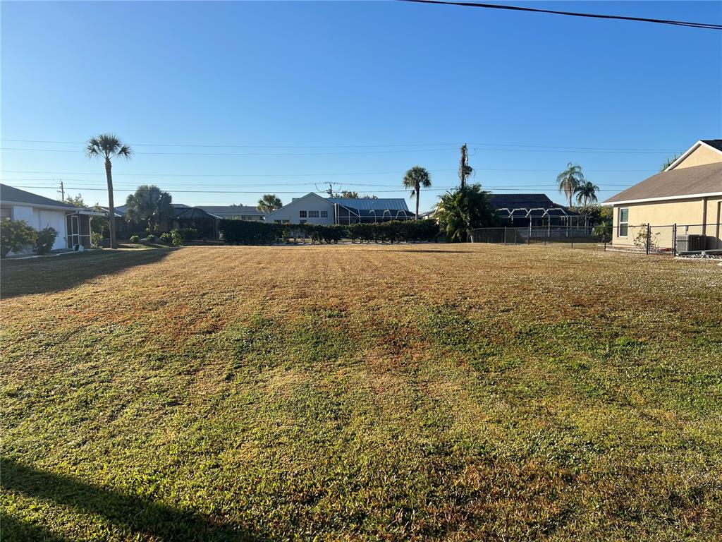 A large, flat, grassy vacant lot is surrounded by residential houses and palm trees — 25285 PADRE LANE, PUNTA GORDA, FL