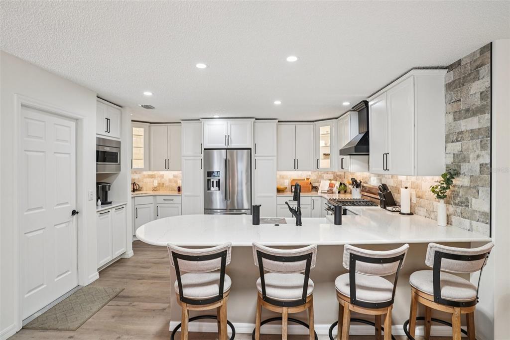 A modern kitchen features white cabinetry, a quartz island with four stools, and stone backsplash — 1609 GIBBES WAY, THE VILLAGES, FL