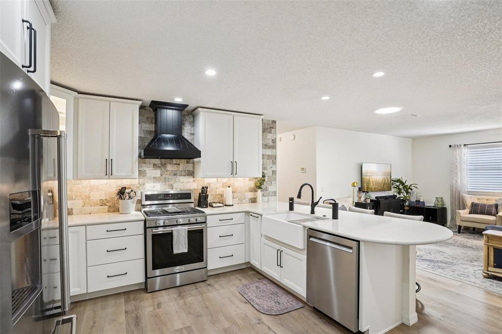 A kitchen with white cabinets, stainless steel appliances, a farmhouse sink, and stone backsplash — 1609 GIBBES WAY, THE VILLAGES, FL