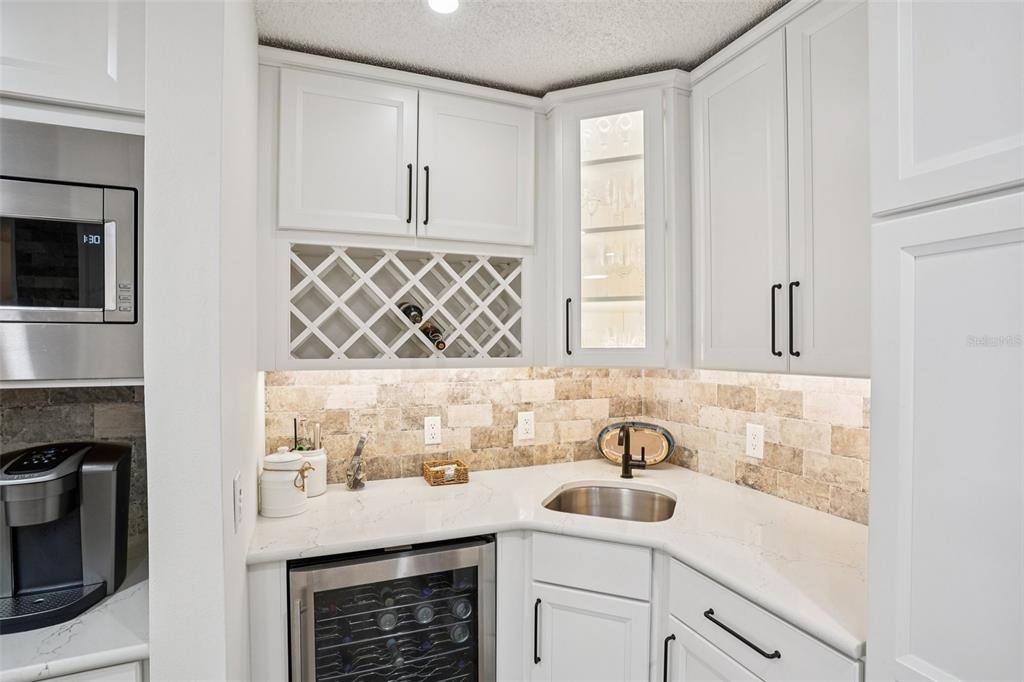 A wet bar features white cabinets, a wine rack, a small sink, and stone backsplash — 1609 GIBBES WAY, THE VILLAGES, FL