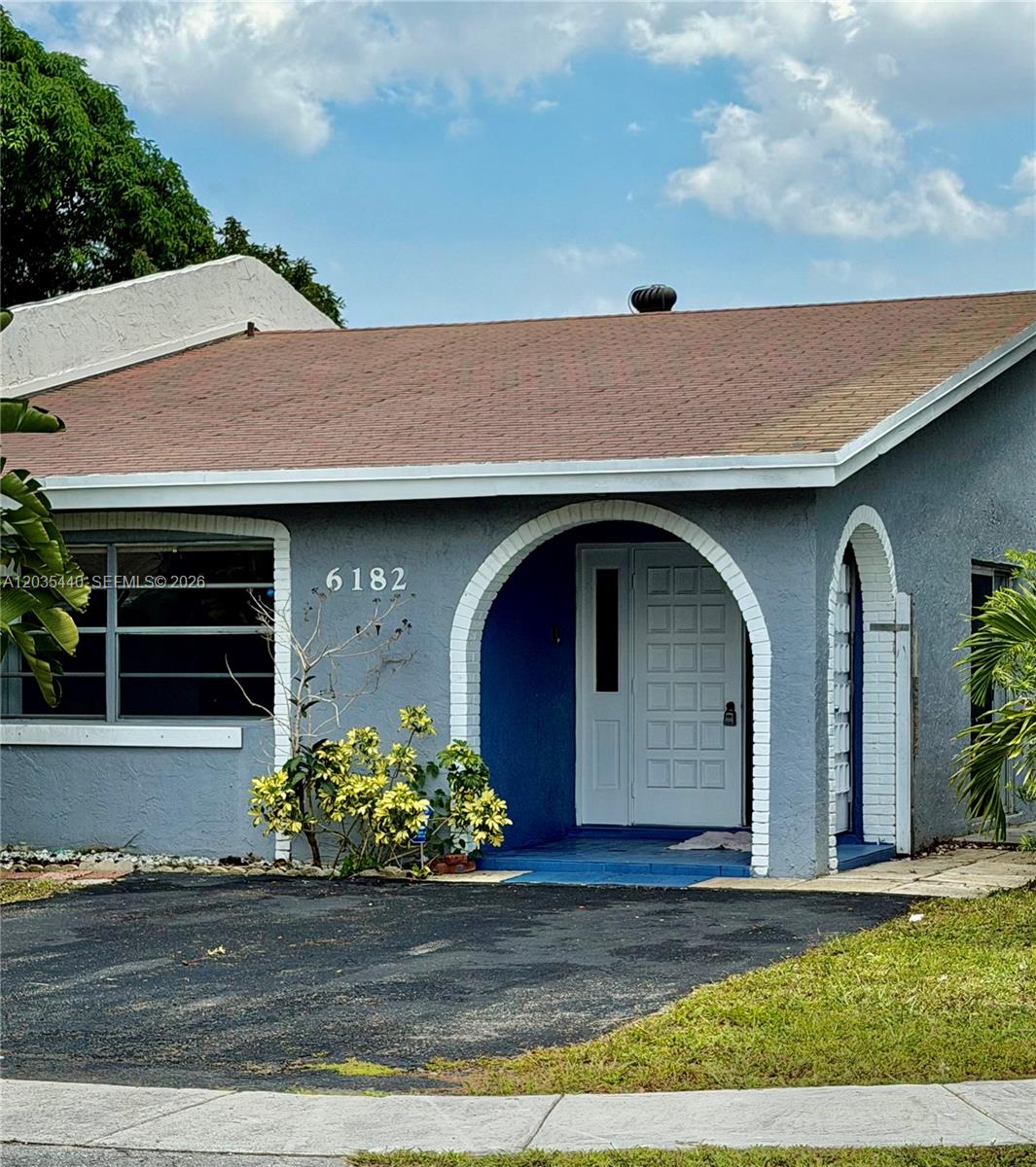 The exterior of a single-story house features a gray facade, arched entryway, and asphalt driveway — 6182 SW 4th St, Margate FL 33068, MARGATE, FL