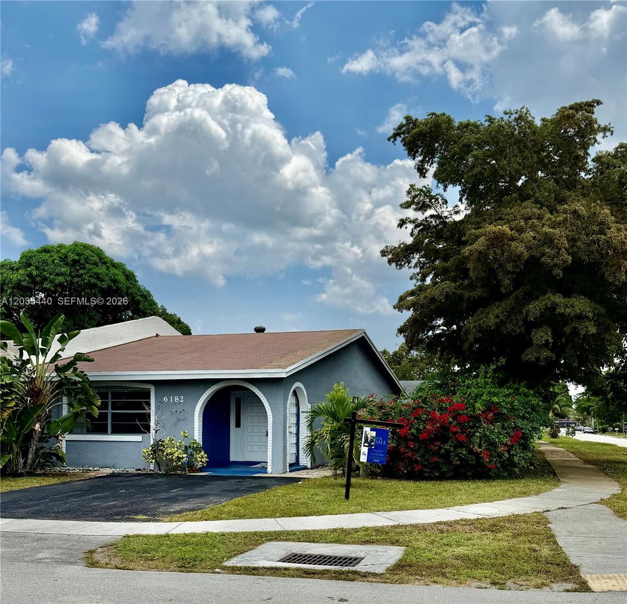 A single-story gray house with a blue arched entryway and a large tree in front — 6182 SW 4th St, Margate FL 33068, MARGATE, FL
