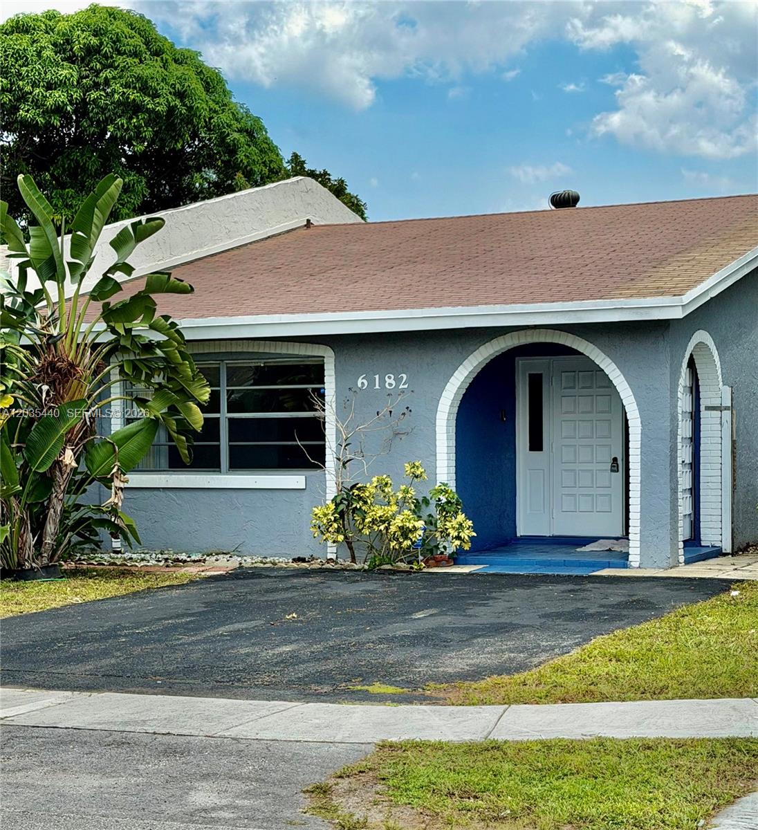 A gray single-story house features a white arched entryway, a driveway, and a large plant — 6182 SW 4th St, Margate FL 33068, MARGATE, FL
