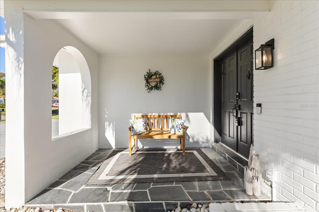 A covered front porch features a stone floor, a wooden bench, and a black door — 13923 BREWSTER DRIVE, LARGO, FL