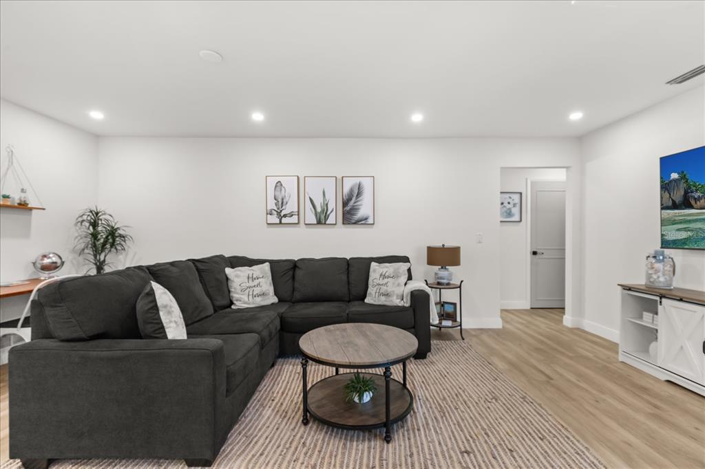 A living room features a dark gray sectional sofa, a round coffee table, and wall art — 13923 BREWSTER DRIVE, LARGO, FL