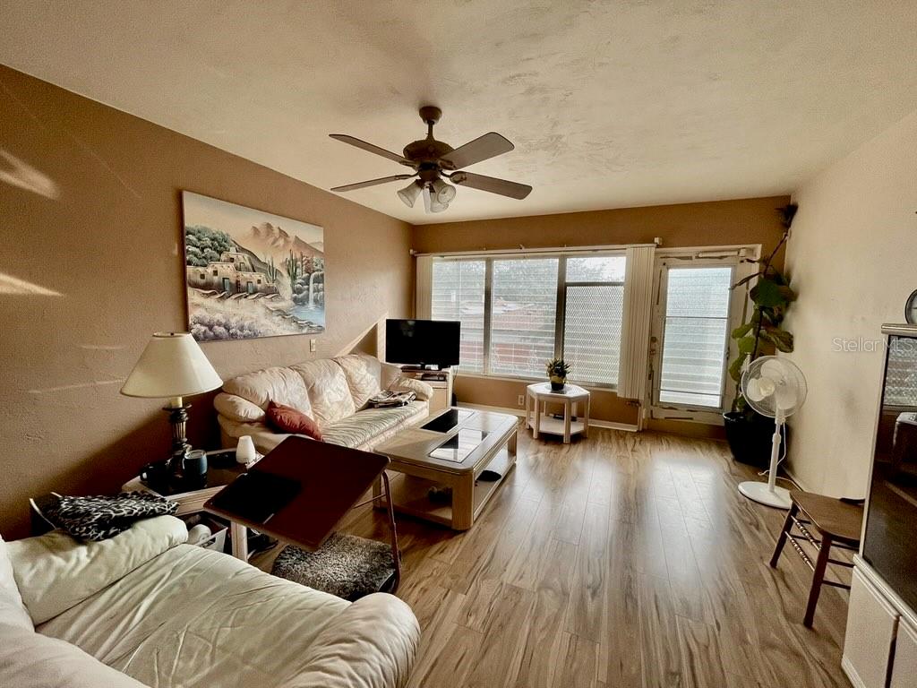 A living room features wood-look flooring, a ceiling fan, a sofa, and large windows — 4060 55TH STREET N UNIT 1209, KENNETH CITY, FL