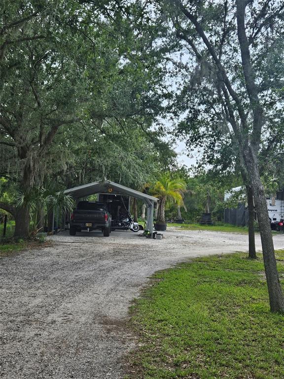 A gravel driveway leads to a metal carport sheltering a truck and a motorcycle — 21910 TAYLOR DRIVE, BRADENTON, FL