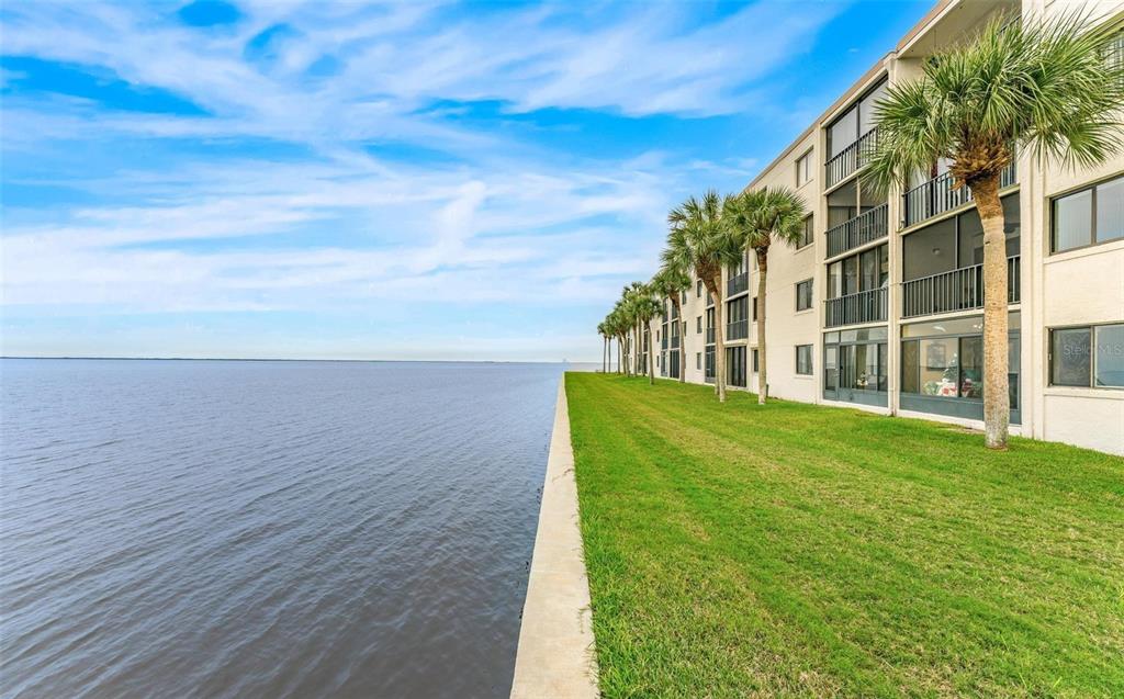 A multi-story apartment building sits beside a large body of water with palm trees — 2465 S WASHINGTON AVENUE UNIT A202, TITUSVILLE, FL