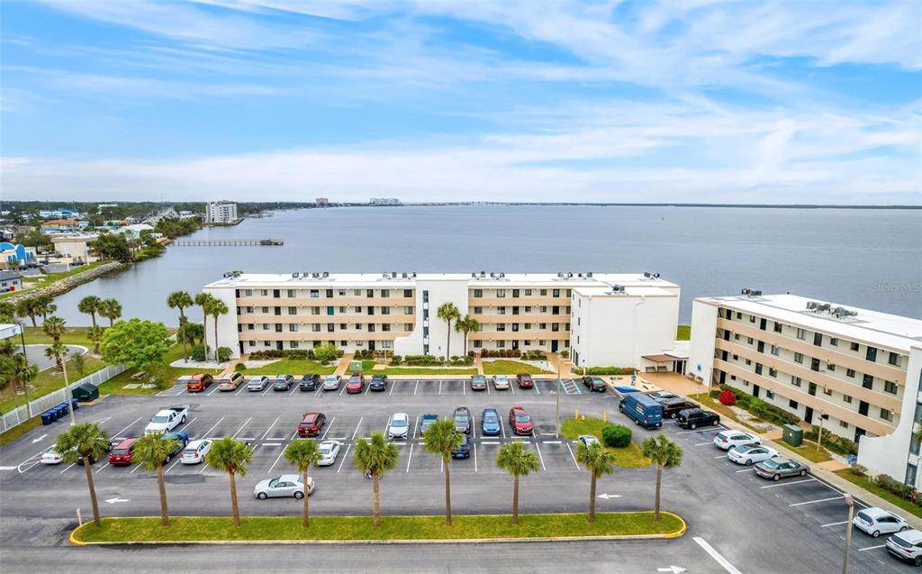 An aerial view shows a multi-story apartment building with a large parking lot and waterfront — 2465 S WASHINGTON AVENUE UNIT A202, TITUSVILLE, FL